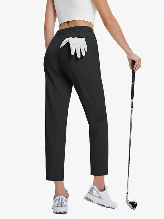 Back lower-body view holding a golf ball with glove in rear pocket wearing BLACK Women's 7/8 Ankle Golf Track Pants.