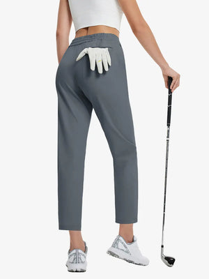 Back lower-body view holding a golf ball with glove in rear pocket wearing DARK GREY Women's 7/8 Ankle Golf Track Pants.
