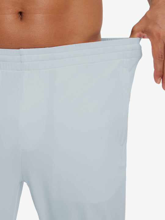 Model stretching waistband to show fit of lightweight traning track pants in misty grey.