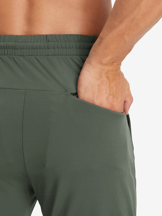 Back view of model with hand in pocket wearing lightweight traning track pants in olive green.
