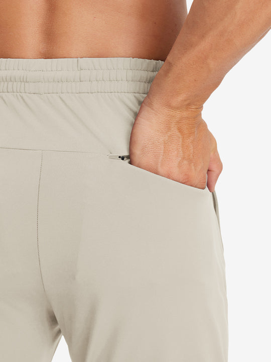 Back view of model with hand in pocket wearing lightweight traning track pants in khaki.
